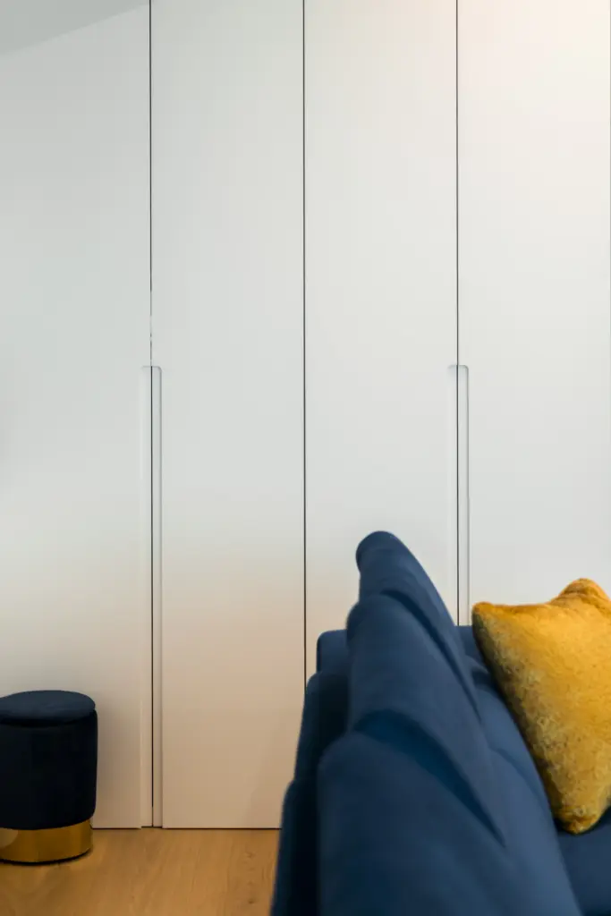 Armadio bianco su misura a filo muro con maniglie integrate, accanto a divano blu e pouf con base oro, realizzato da Ebanisteria Stasi