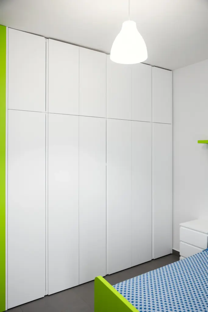 Armadio bianco su misura in una cameretta moderna con letto verde.