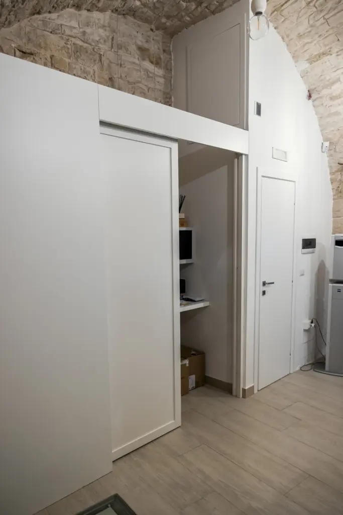 Armadio bianco su misura con porta scorrevole, realizzato all'interno di una nicchia con volta in pietra.