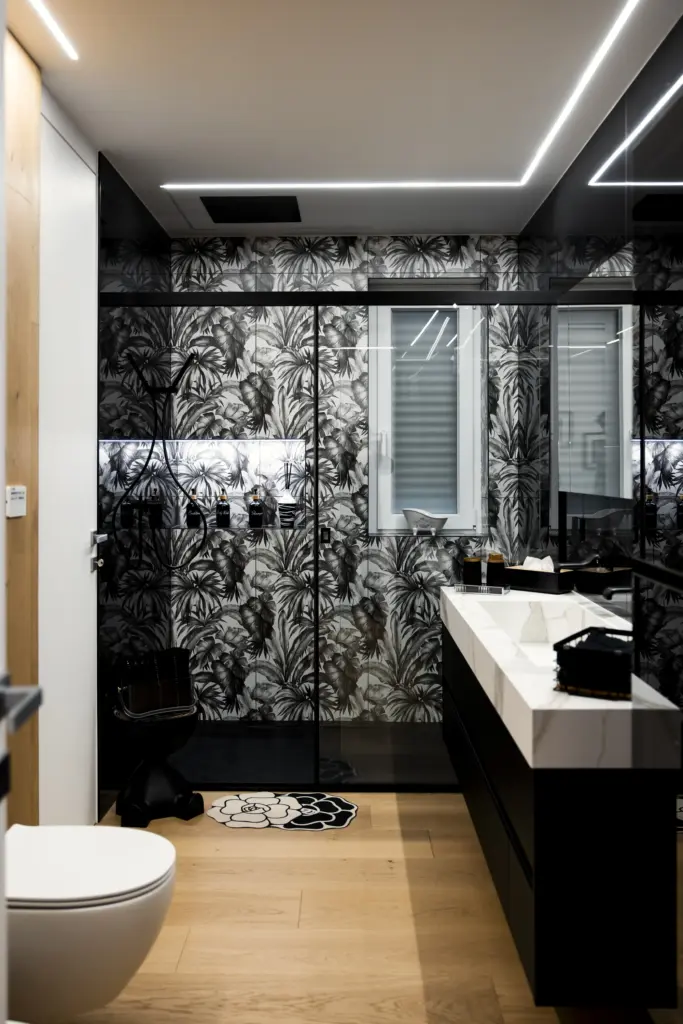 Bagno moderno con pareti rivestite in carta da parati tropicale in bianco e nero, mobile bagno con top in marmo e illuminazione LED integrata