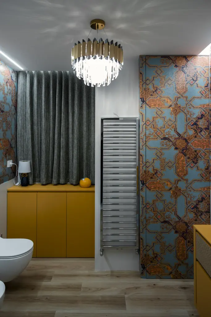 Bagno moderno con mobili color senape, lampadario di design e piastrelle decorative blu e rame.