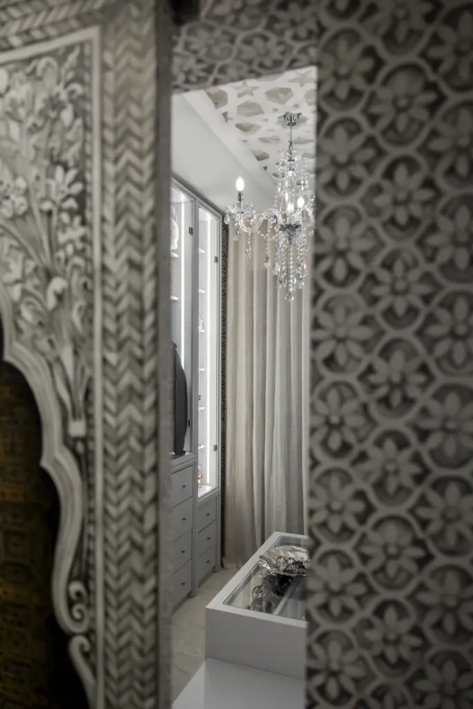 Riflesso di una cabina armadio di lusso con specchio decorato, lampadario in cristallo e arredi su misura in stile elegante.