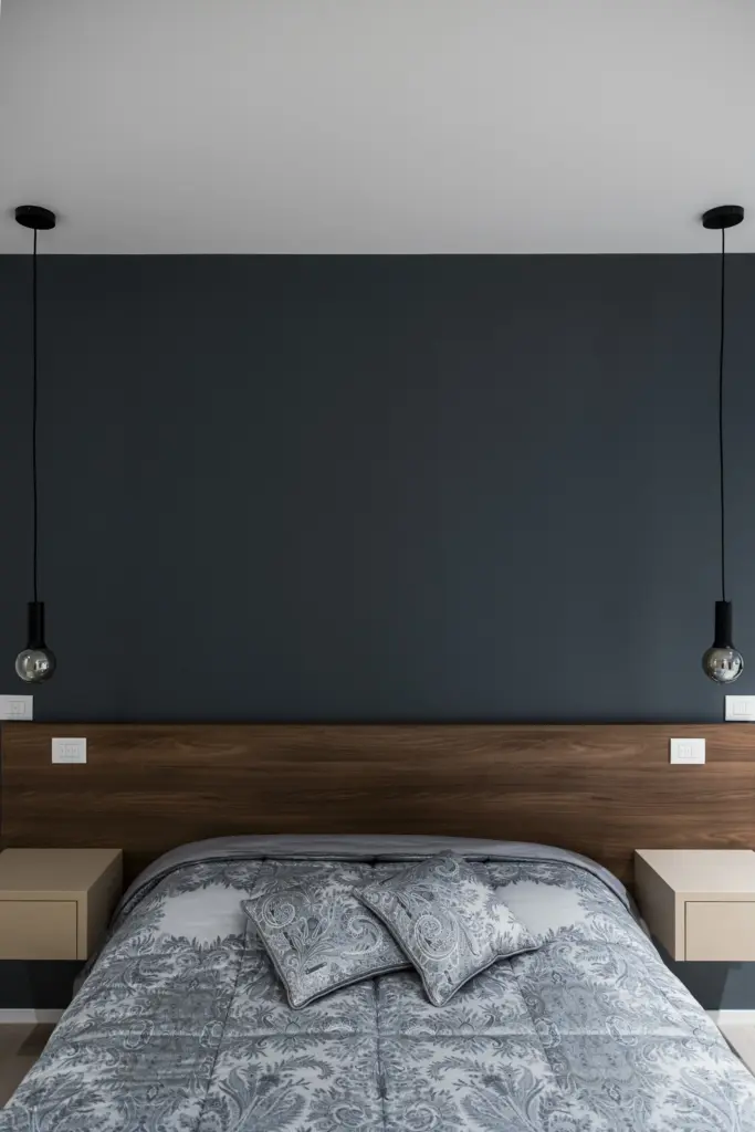 Letto matrimoniale moderno con testiera in legno, comodini sospesi beige e lampade pendenti nere.