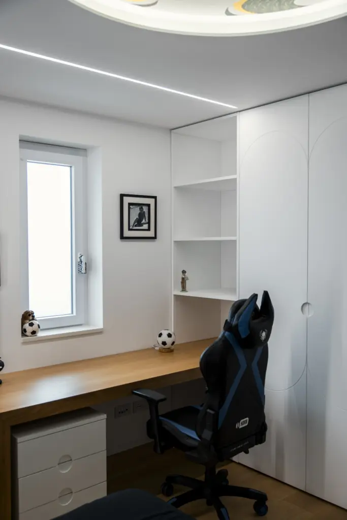 Camera da studio per ragazzo con scrivania in legno, sedia da gaming e armadio bianco integrato.