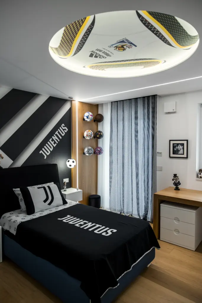 Camera da letto moderna con arredamento personalizzato a tema Juventus, decorazioni calcistiche e letto singolo.