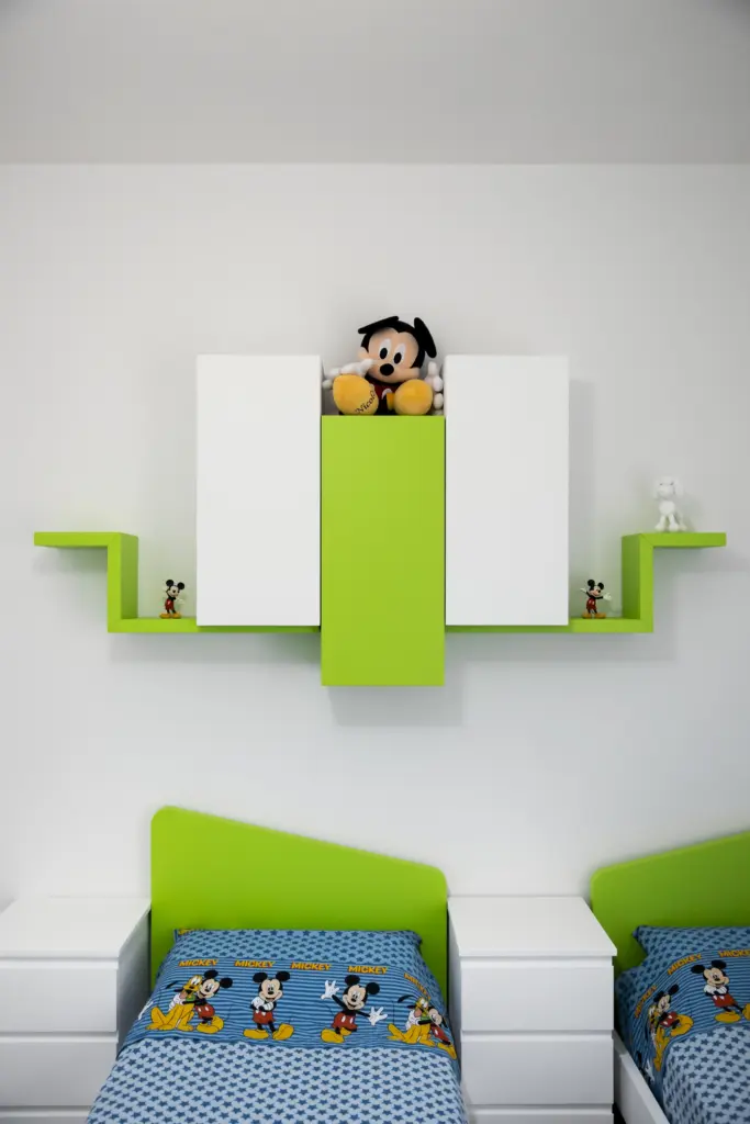 Cameretta per bambini con mobili verdi e bianchi e letti singoli con testiera colorata.