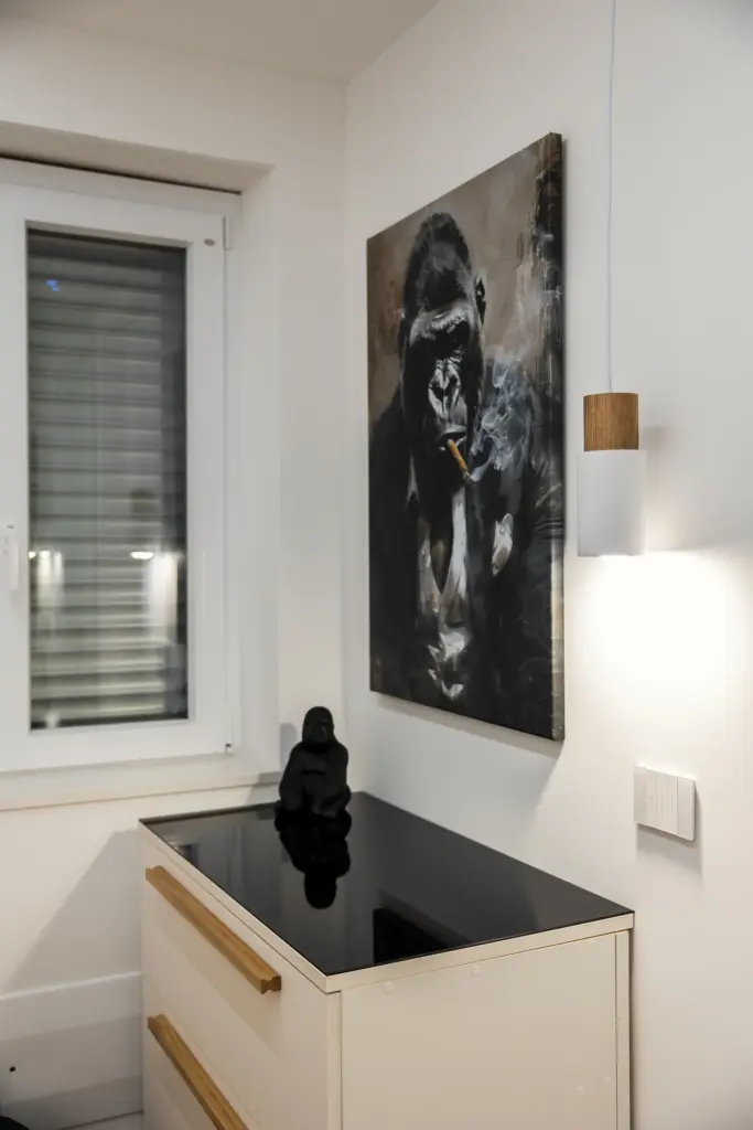 Cassettiera bianca con piano in vetro nero e maniglie in legno naturale, accanto a quadro decorativo moderno.