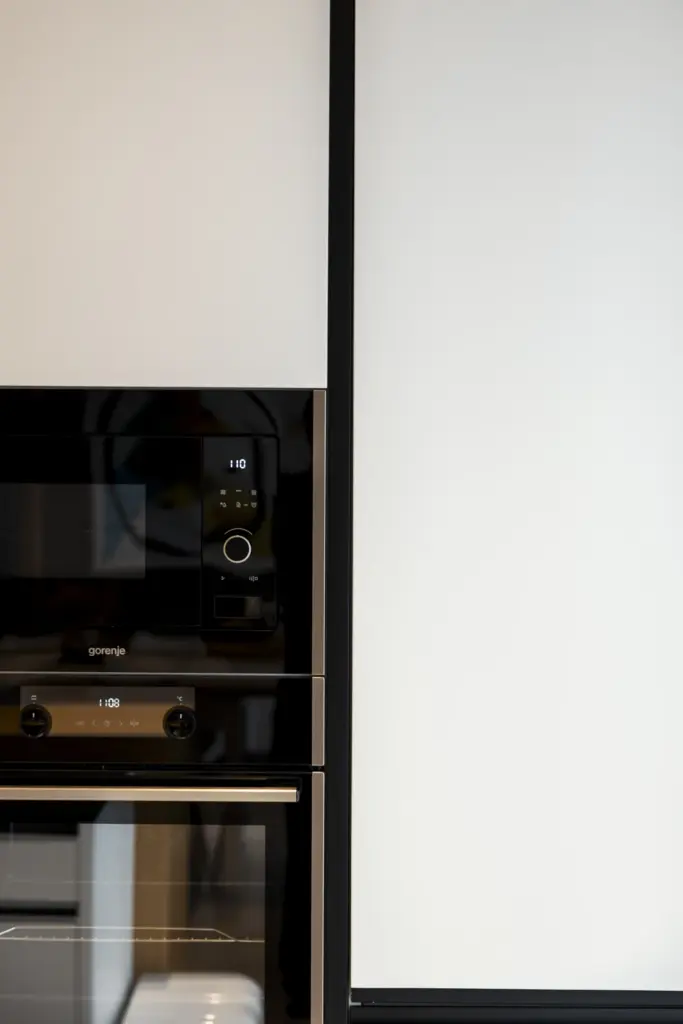 Colonna attrezzata di cucina moderna con forno e microonde a incasso, finitura bianca opaca e dettagli neri.