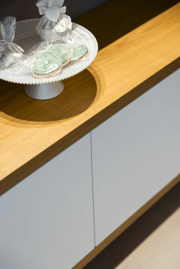 Dettaglio di credenza moderna in legno chiaro e ante bianche con vassoio di dolcetti.