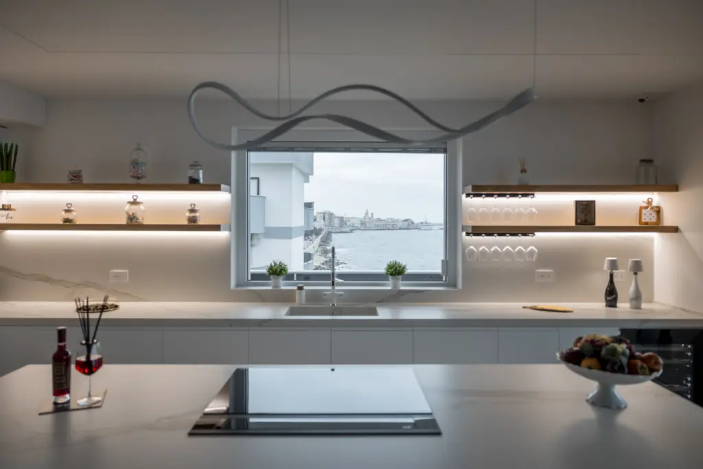 Cucina moderna con isola centrale, mensole retroilluminate e ampia finestra con vista sul mare