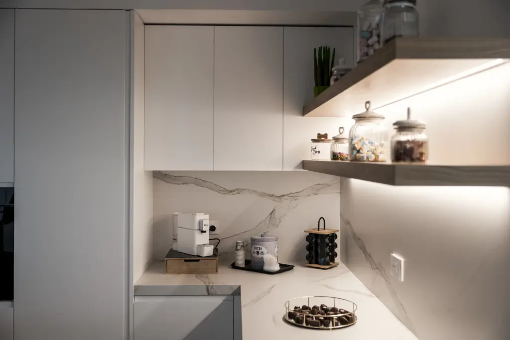 Dettaglio di cucina moderna con angolo caffè, mensole in legno retroilluminate e piano effetto marmo.