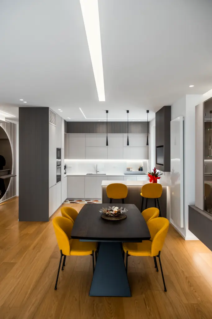 Cucina moderna total white con isola centrale, pensili a scomparsa e zona pranzo con sedie gialle e tavolo nero