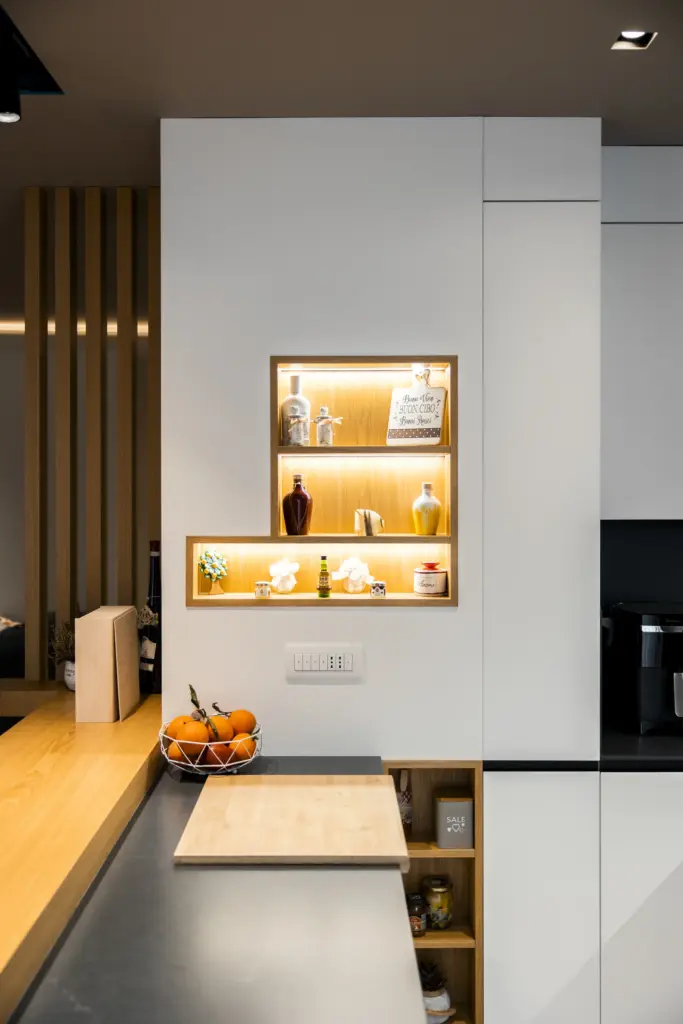 Dettaglio di cucina moderna con nicchia in legno illuminata, arredo bianco e piano in marmo scuro.