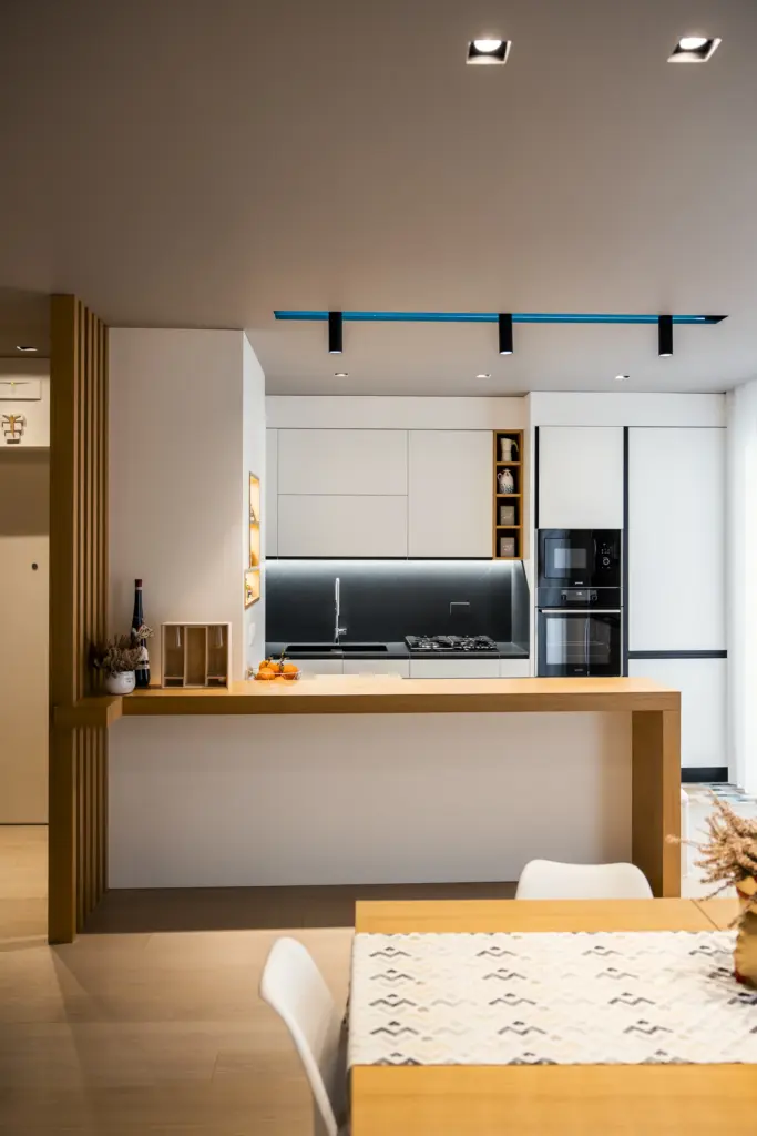 Cucina moderna con penisola in legno naturale, mobili bianchi e dettagli neri, design elegante e minimalista.