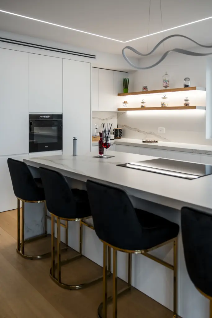 Cucina bianca moderna con isola centrale, piano cottura a induzione e sgabelli neri con struttura dorata.