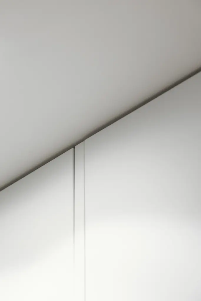 Dettaglio di ante sagomate bianche che seguono la pendenza del soffitto.
