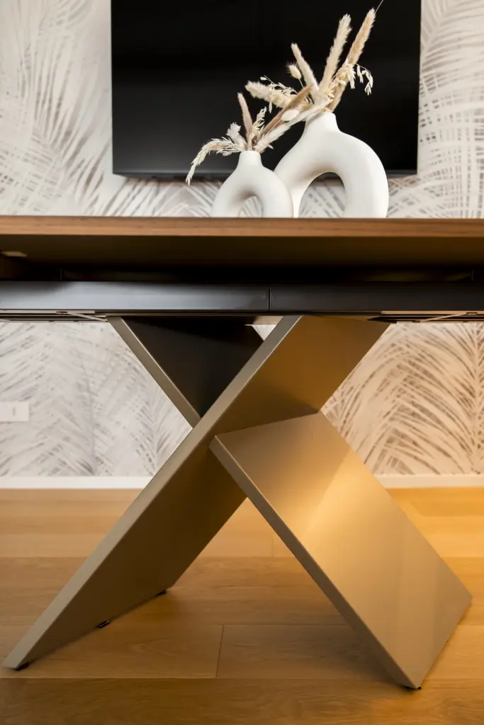 Dettaglio della base incrociata di un tavolo in metallo verniciato, con piano in legno e decorazione in stile minimal
