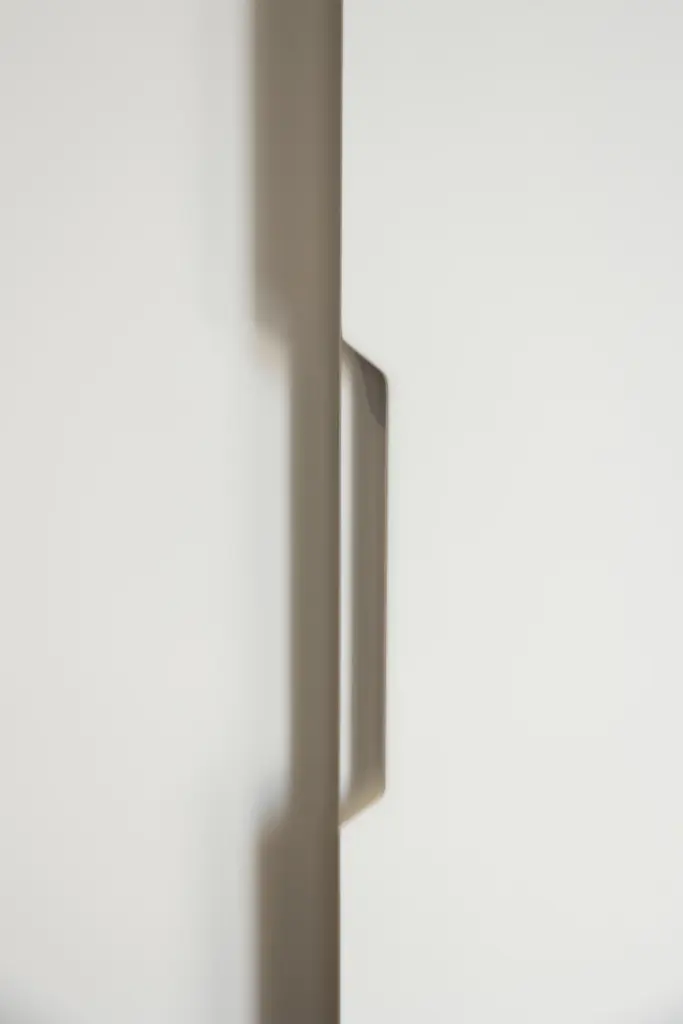 Maniglia minimalista in metallo satinato applicata su anta bianca.