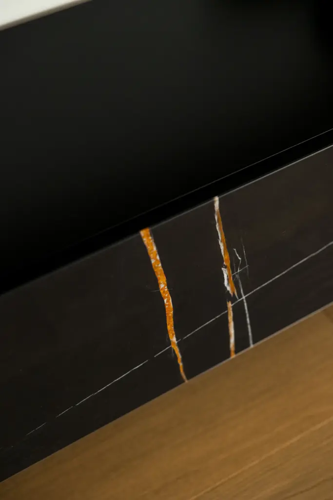 Dettaglio di un mobile moderno con frontale in marmo scuro venato arancio e vetro nero opaco, su pavimento in legno naturale