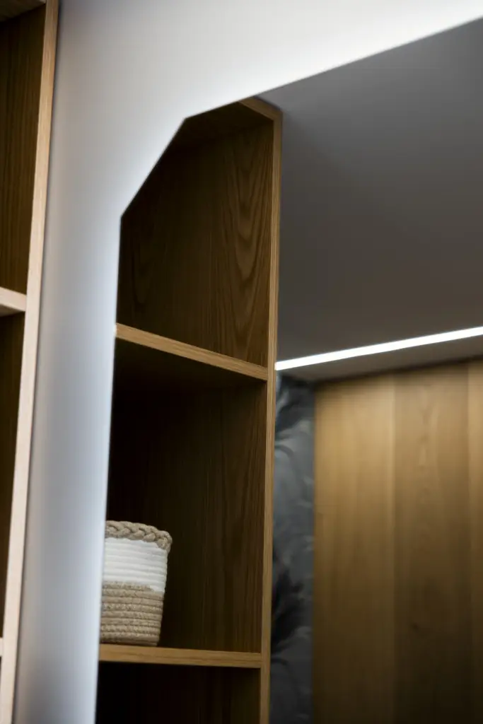Dettaglio di mobile bagno in legno naturale con ripiani aperti e illuminazione LED.