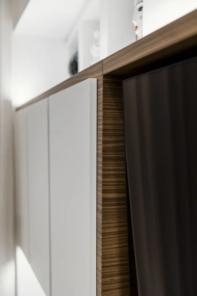 Particolare di una parete attrezzata moderna con finiture in legno naturale e ante bianche opache.