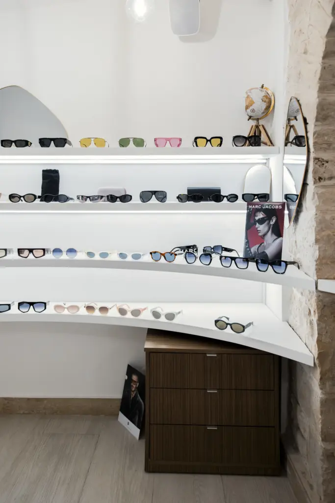 Espositore da ottica con ripiani curvi retroilluminati e occhiali da sole in mostra, accompagnato da cassettiere in legno.