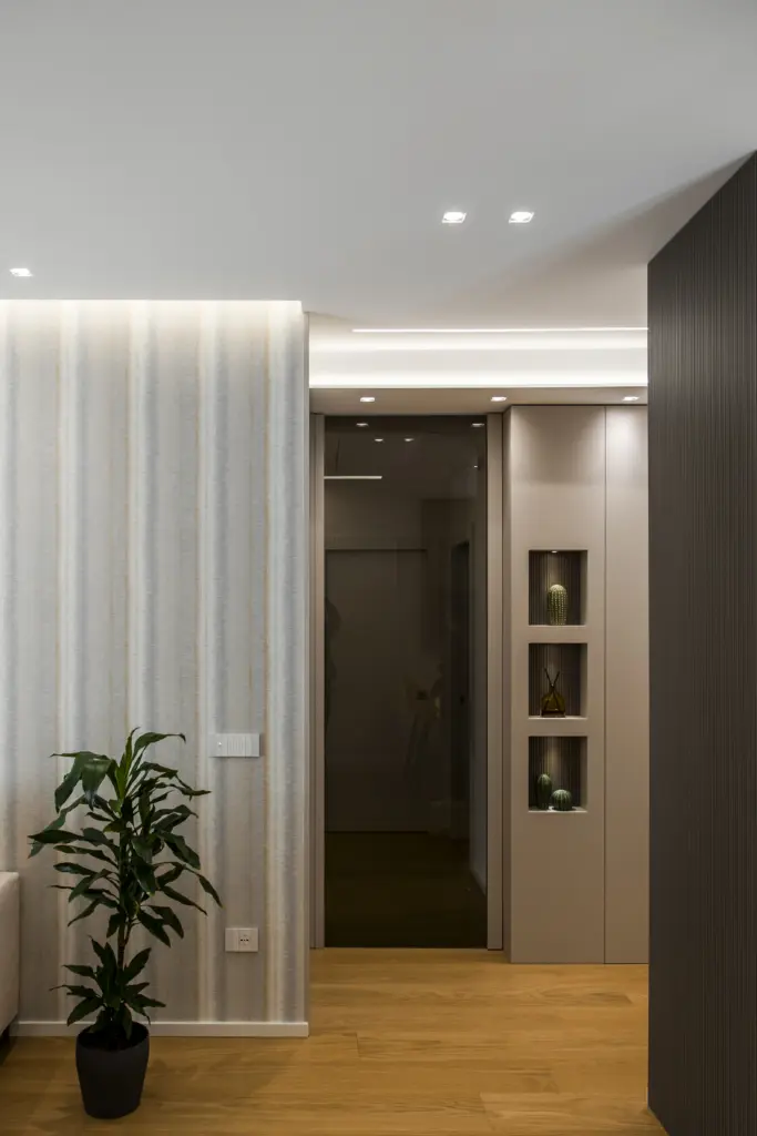 Elegante ingresso moderno con porta a specchio scuro, armadio grigio con nicchie decorative contenenti piante grasse, illuminazione LED e pavimento in legno.
