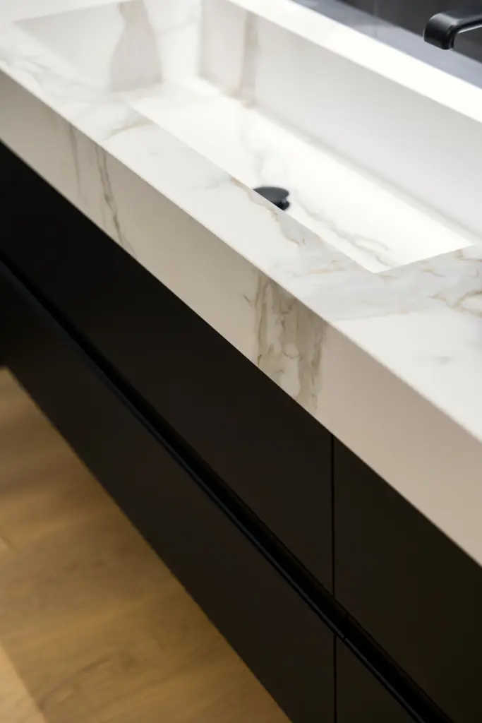 Dettaglio laterale di lavabo integrato in marmo con venature naturali e base nera opaca, design su misura per bagno moderno