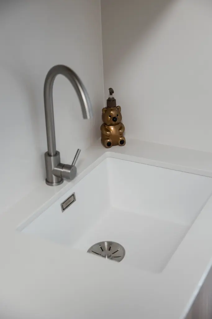 Lavello ad incasso bianco con rubinetto in acciaio satinato e dispenser decorativo a forma di orsetto.