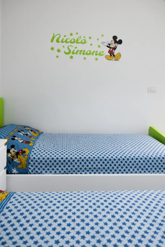 Letti singoli bianchi con testiera verde e biancheria tema Disney.