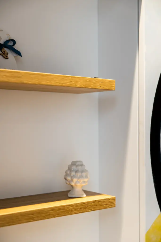 Dettaglio di mensole in legno con piccolo oggetto decorativo in ceramica bianca.