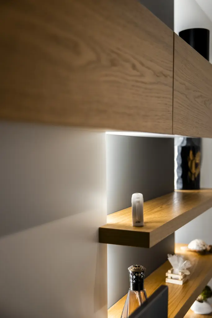 Dettaglio di mensole in legno con luci integrate su parete bicolore.