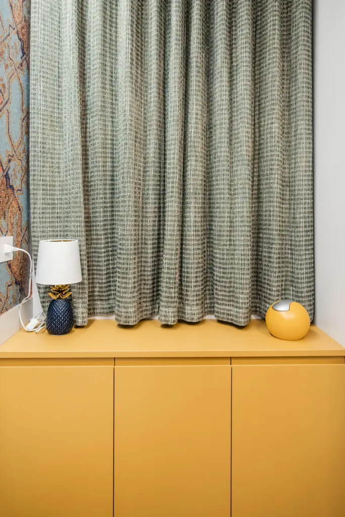 Dettaglio di un mobile bagno moderno color senape con tende in tessuto decorativo e accessori d'arredo.