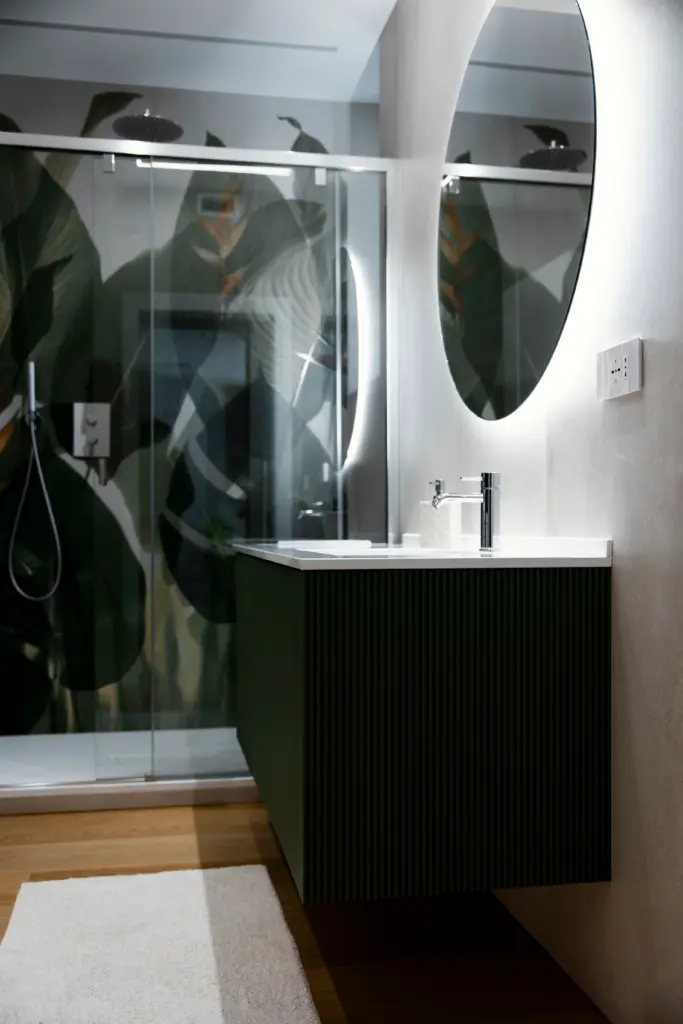 Mobile bagno sospeso verde cannettato con lavabo bianco integrato, specchio retroilluminato e doccia con parete decorativa a foglie
