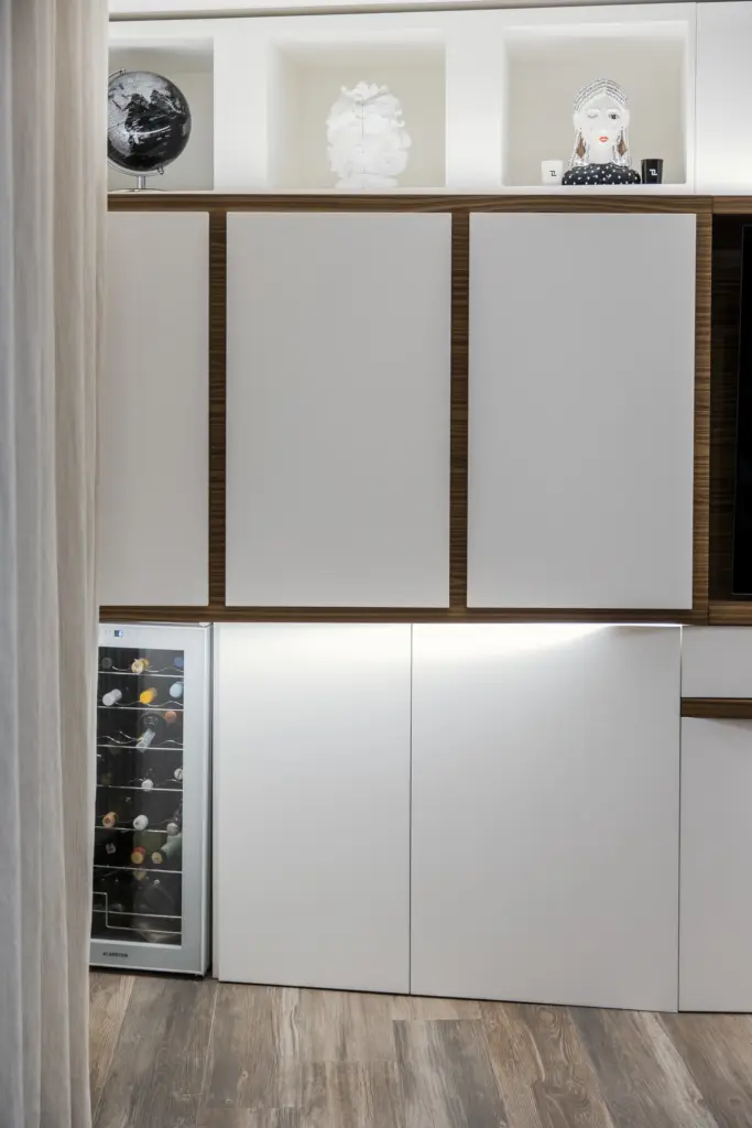 Mobile da soggiorno moderno in bianco e legno, con vetrinetta refrigerata per vini e nicchie illuminate.