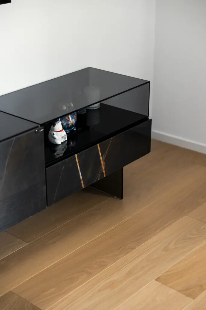 Mobile sospeso con finiture in marmo venato e vetro nero, su pavimento in legno chiaro, con oggetti decorativi all’interno