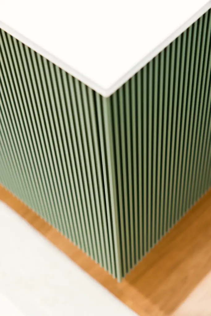 Primo piano su mobile moderno con finitura cannettata verde e top bianco, su pavimento in legno chiaro