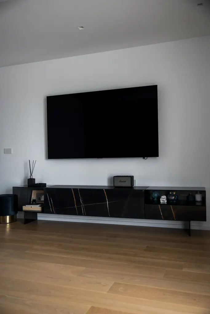 Mobile TV sospeso con finiture in marmo e vetro nero, posizionato sotto un televisore a parete su fondo bianco