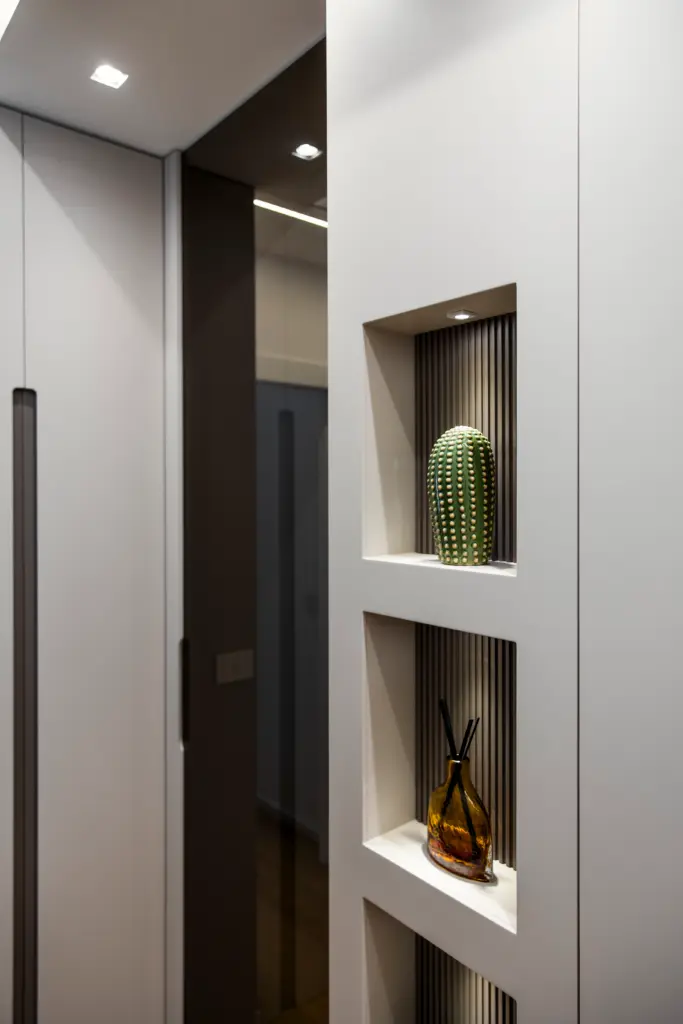 Parete con nicchie decorative retroilluminate e pannello dogato, contenente oggetti di design come cactus in ceramica e diffusore di essenze