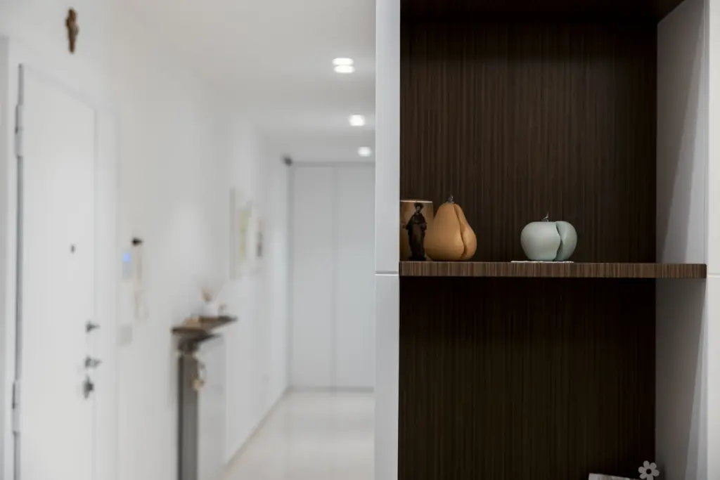 Mensole in legno scuro con oggetti decorativi all'interno di una nicchia in un ingresso moderno.