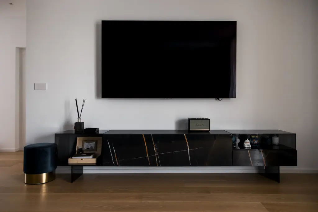 Parete soggiorno con TV a muro e mobile sospeso in marmo venato e vetro, su pavimento in legno chiaro