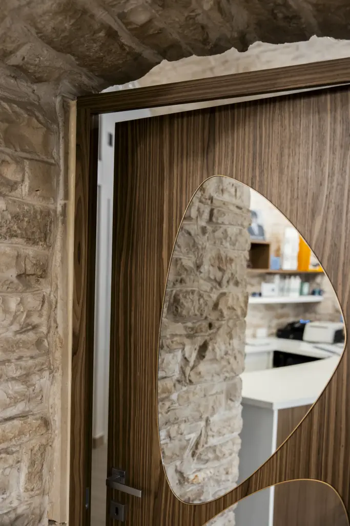 Porta in legno di noce con inserto in vetro sagomato, incorniciata da pareti in pietra viva.