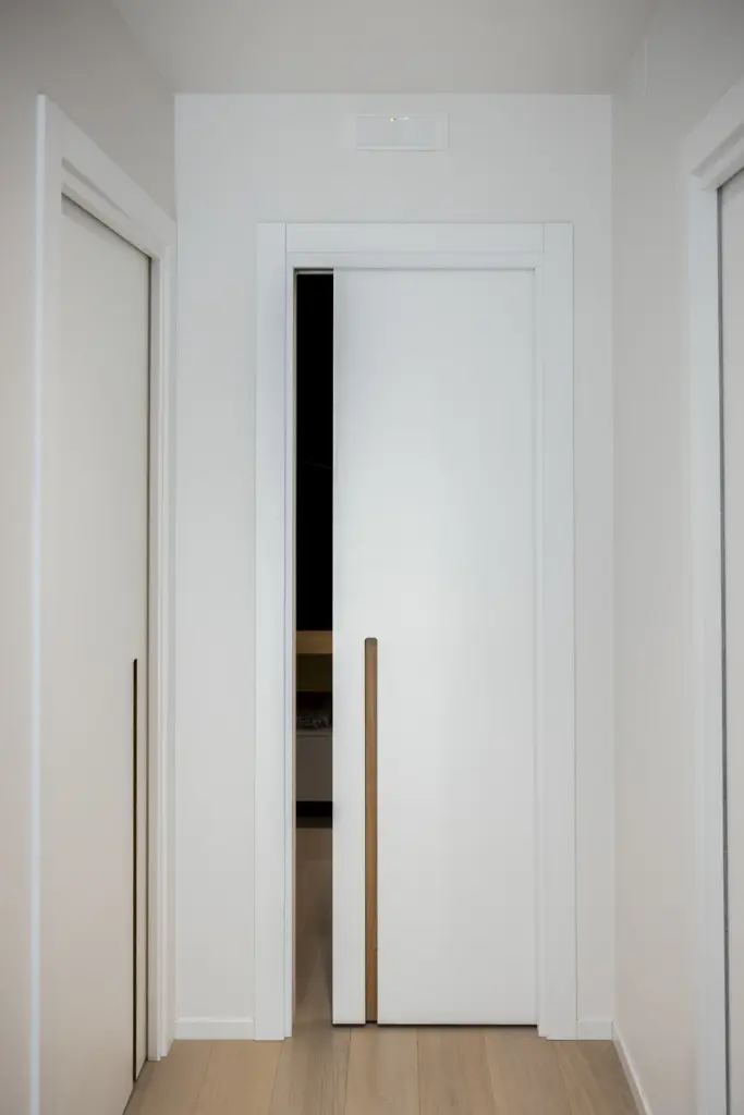 Porta bianca scorrevole con maniglia verticale in legno integrata, design moderno per interni.