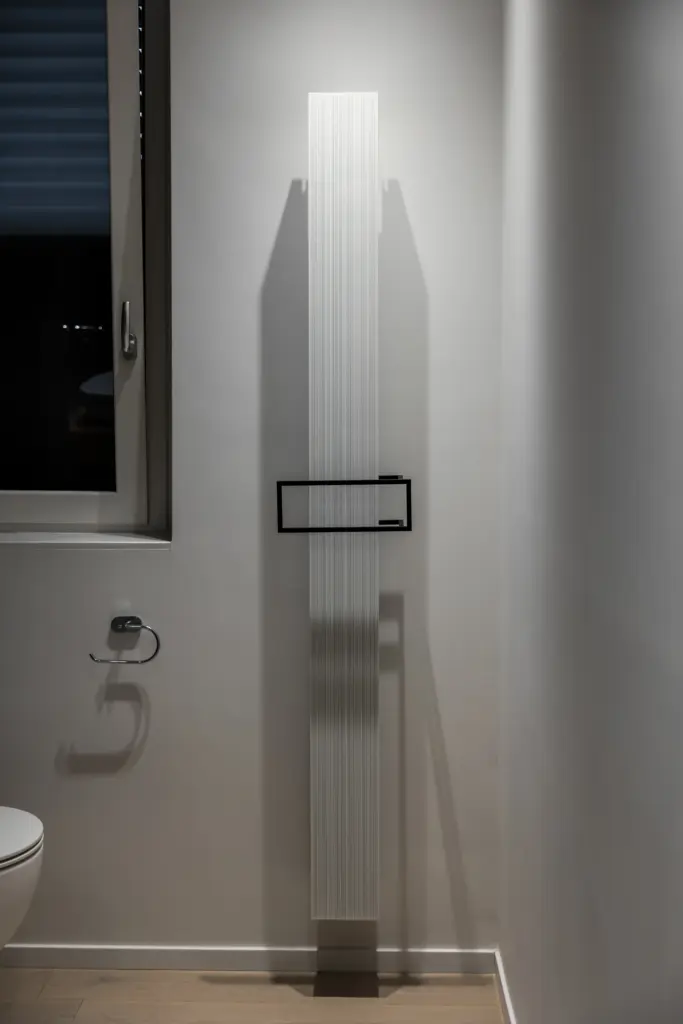 Radiatore verticale in vetro con maniglia rettangolare nera installato in bagno moderno.