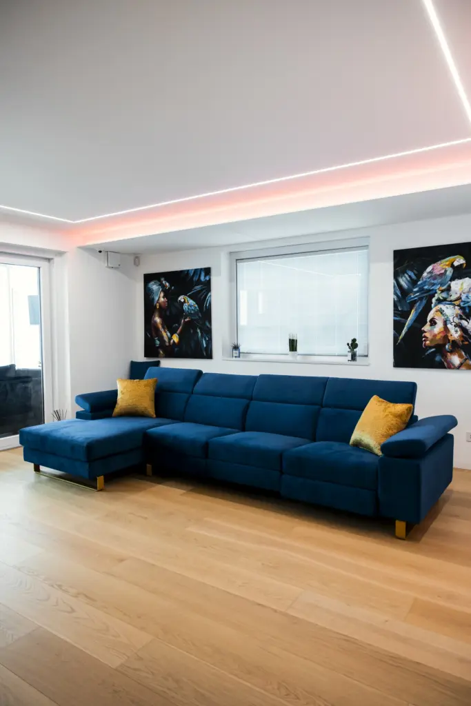 Salotto contemporaneo con divano angolare blu, parquet chiaro e illuminazione LED a soffitto.