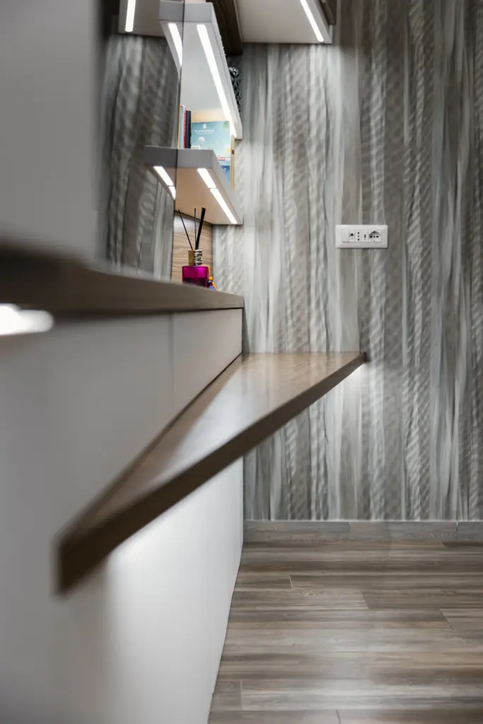 Piano in legno naturale con mensole bianche illuminate a LED in una libreria moderna su misura, sfondo con carta da parati a motivi verticali.