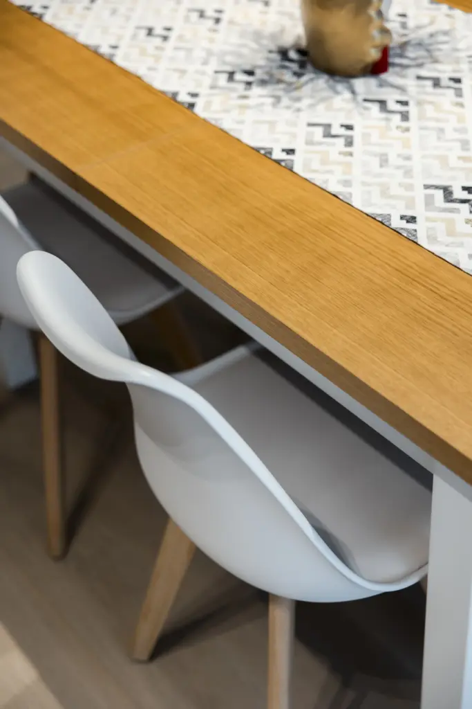 Dettaglio di tavolo in legno chiaro con sedie bianche moderne.
