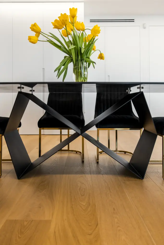 Tavolo moderno con piano in vetro e base in metallo nero, decorato con tulipani gialli in soggiorno luminoso.
