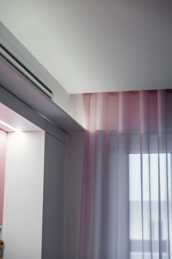 Tendaggi rosa leggeri in una camera da ragazza moderna, con arredi bianchi e illuminazione soffusa.