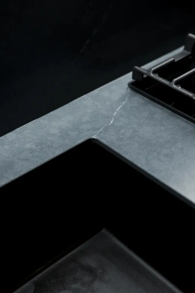 Dettaglio di top cucina moderno in materiale scuro con venatura chiara e piano cottura integrato.